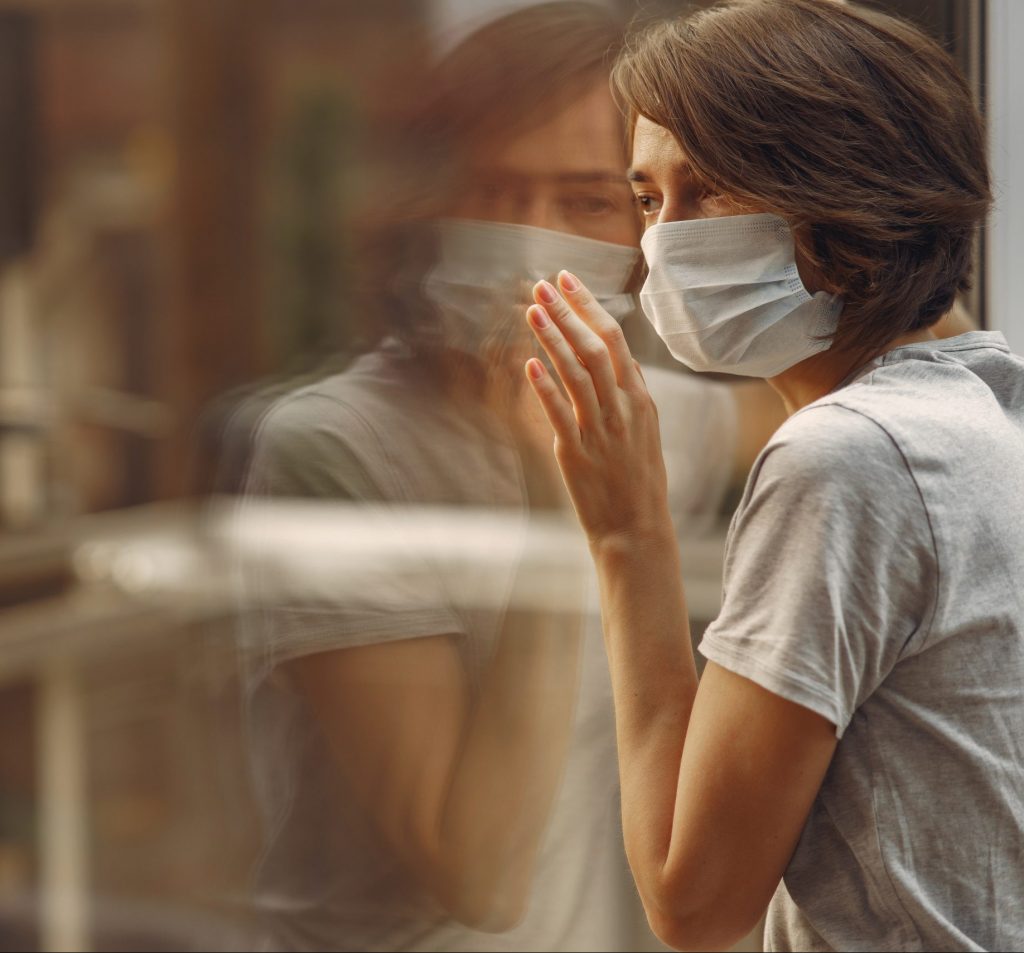 Mujer con máscara médica parada junto a la ventana